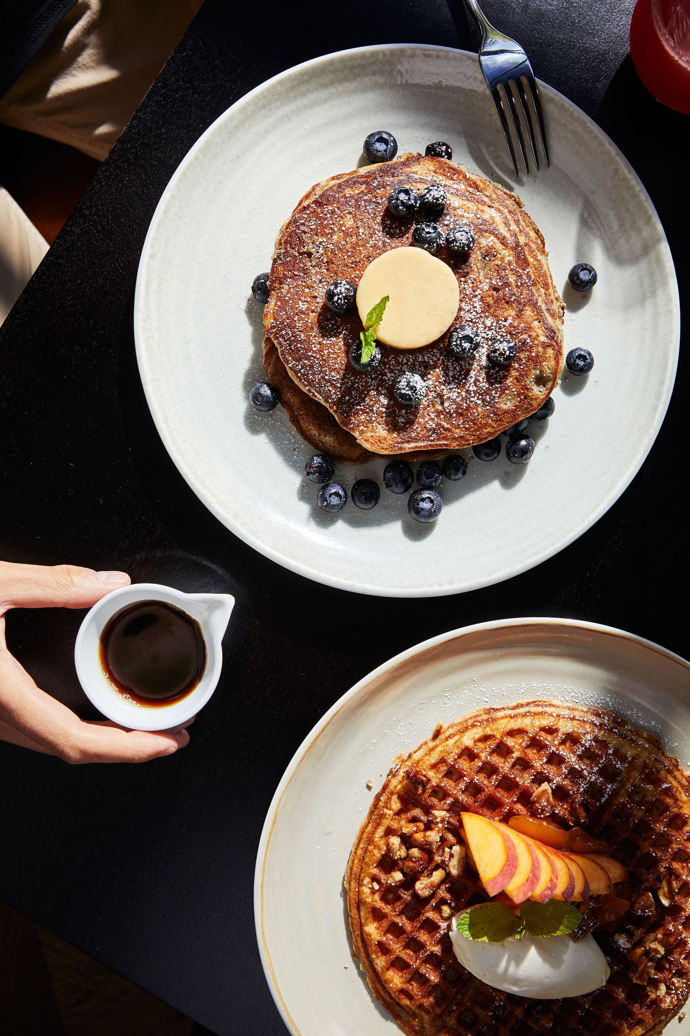 A breakfast setting with pancakes on plates, blueberries, and a small cup of syrup.