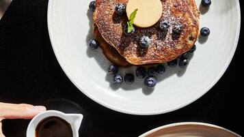 A breakfast setting with pancakes on plates, blueberries, and a small cup of syrup.