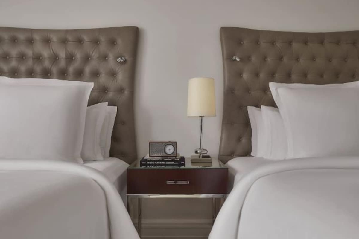 A hotel room with two beds, a nightstand with a lamp, and a radio.