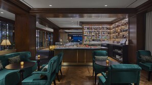 A bar area with a wooden bar counter, shelves of bottles, and teal upholstered seating. - Rosewood Washington, D.C. (Washington)