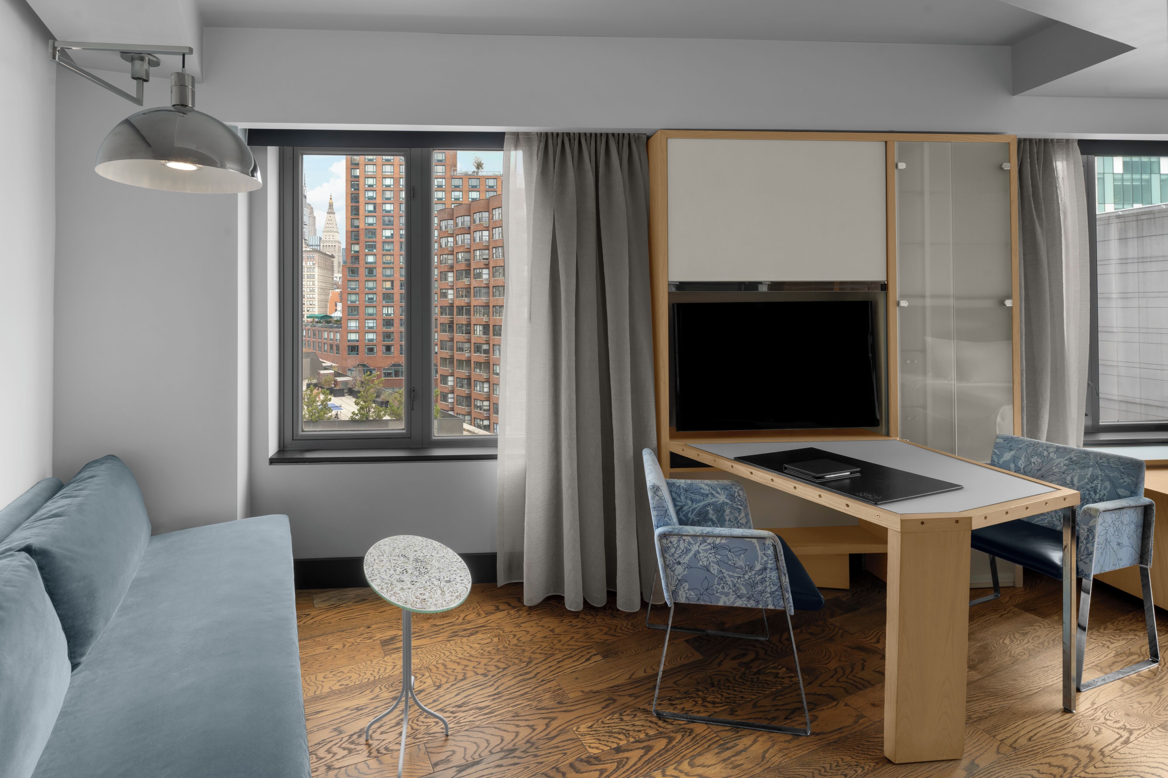 A modern room with a sofa, a dining table with chairs, a TV, and a large window with curtains.