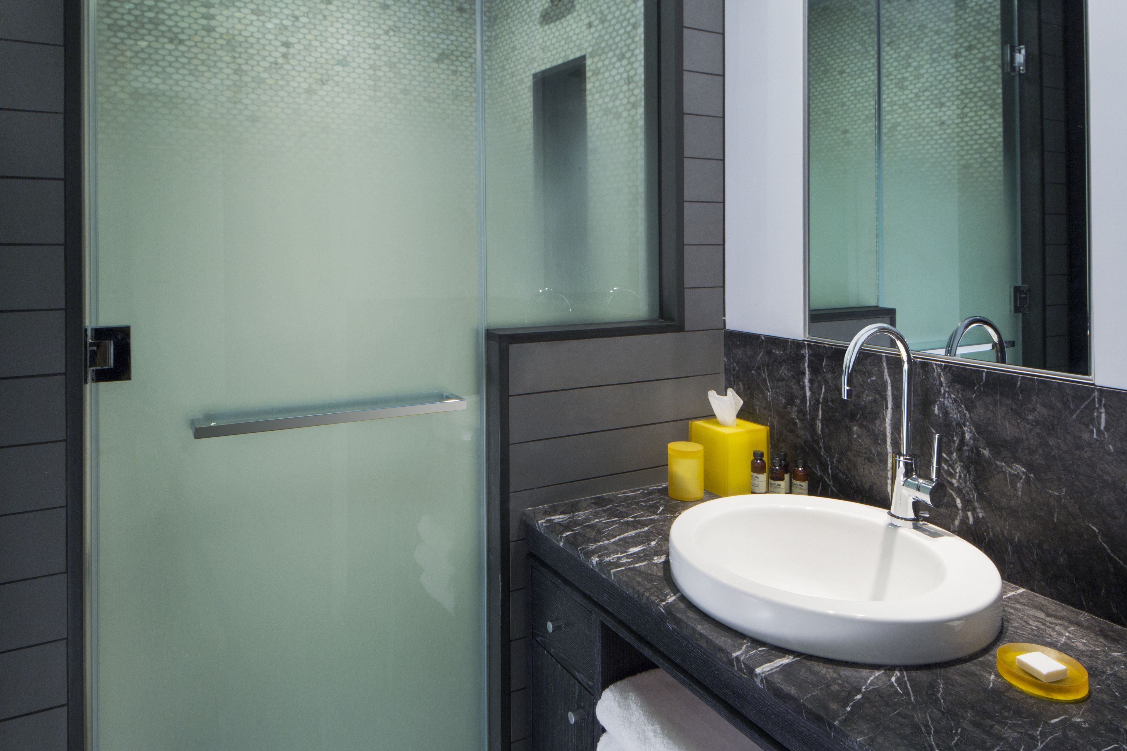 A modern bathroom with a glass shower enclosure, a white sink, and a marble countertop.