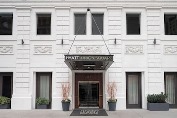 A modern hotel room with a bed, a desk, a chair, a hanging light fixture, and a balcony with outdoor furniture and plants. at Hyatt Union Square New York