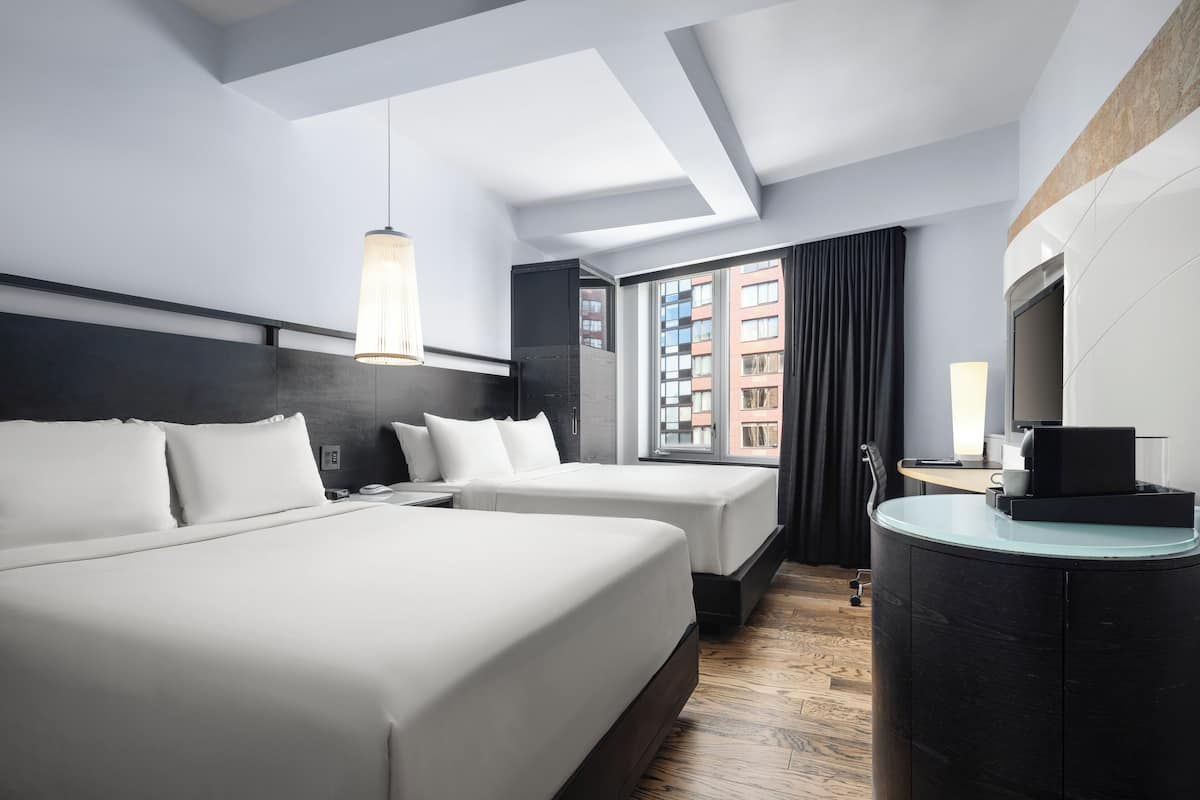 Una habitación de hotel moderna con dos camas, un escritorio, un televisor y un ventanal grande.