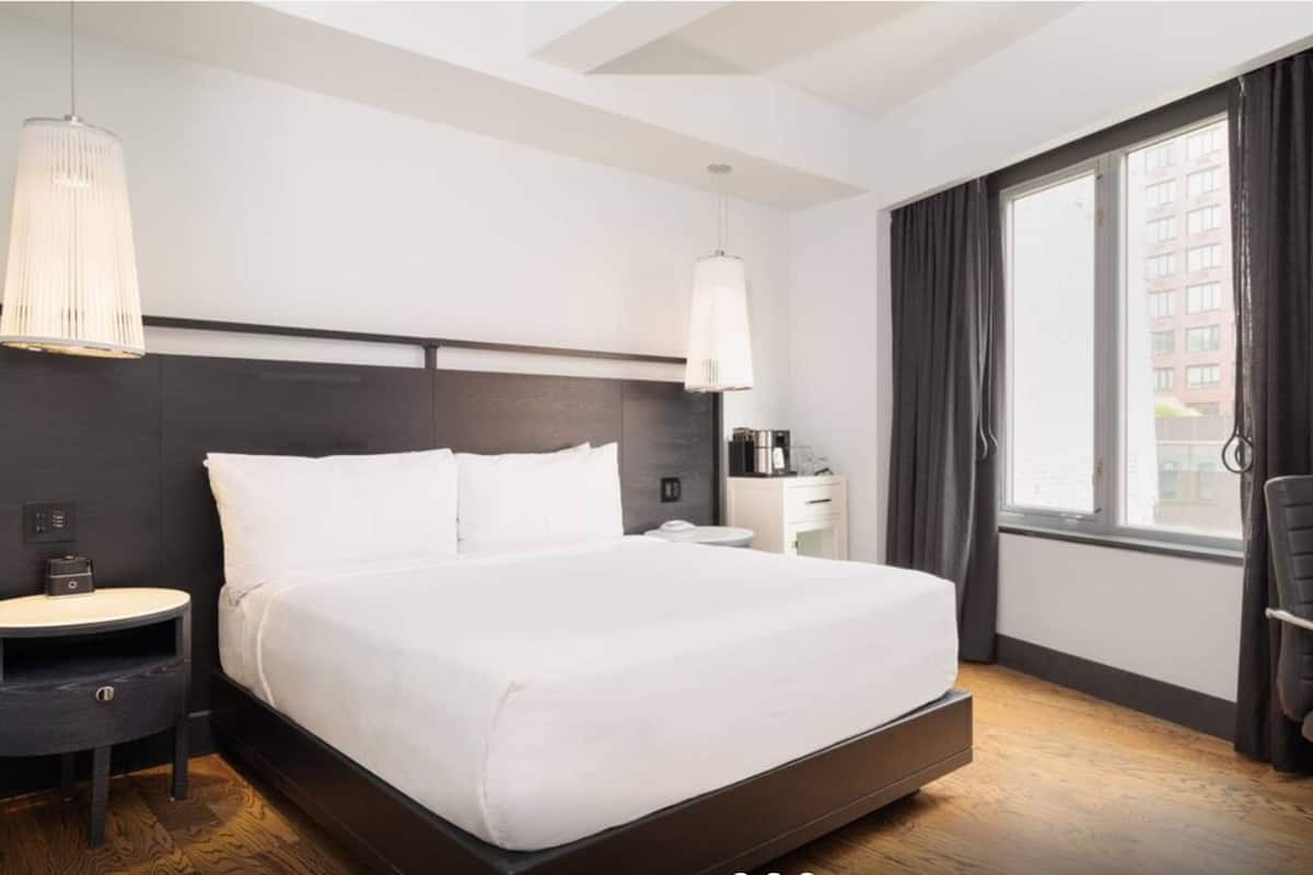 Habitación de hotel con una cama grande, un escritorio, una silla, una cafetera y una ventana con cortinas.