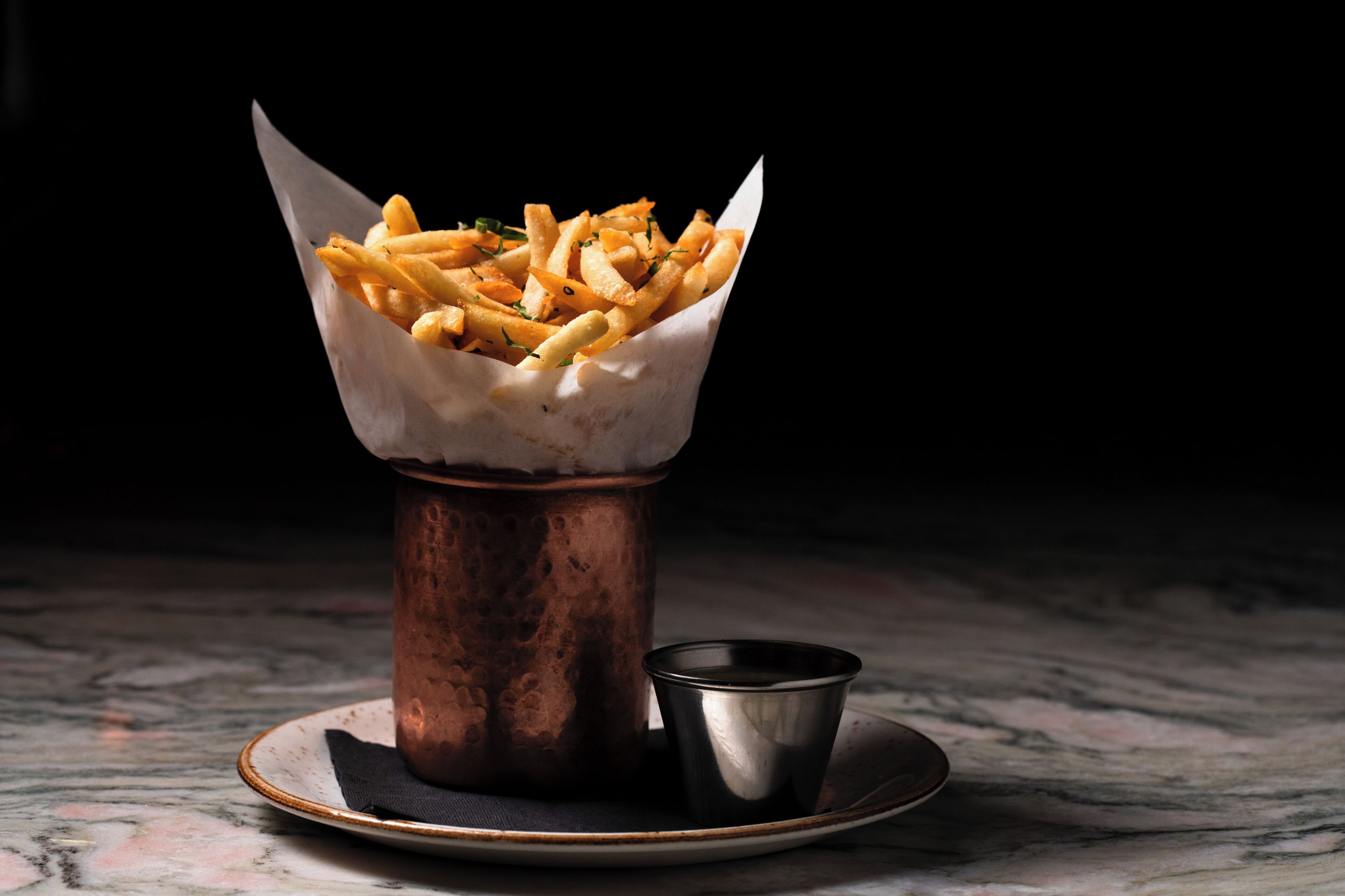 Un récipient en cuivre contenant des frites, disposées sur une assiette.