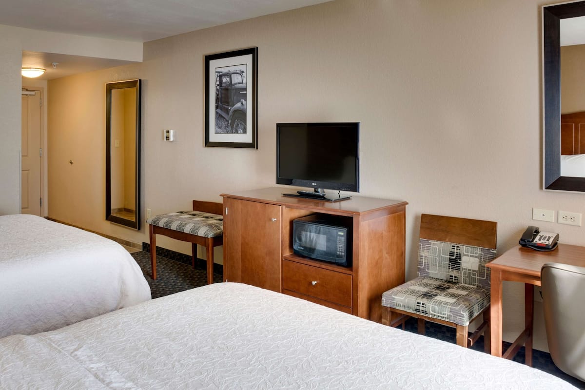 A hotel room with two beds, a television, a microwave, a desk with a chair, and a framed picture on the wall.