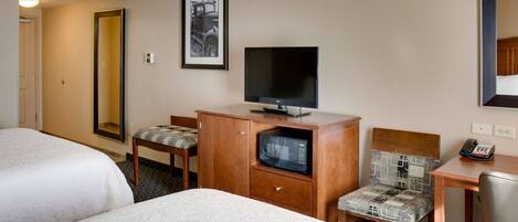Habitación de hotel con dos camas, televisión, microondas, escritorio con silla y un cuadro en la pared.