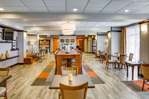 Un amplio vestíbulo de hotel con zona de comedor central, varios conjuntos de asientos y una lámpara de araña moderna.