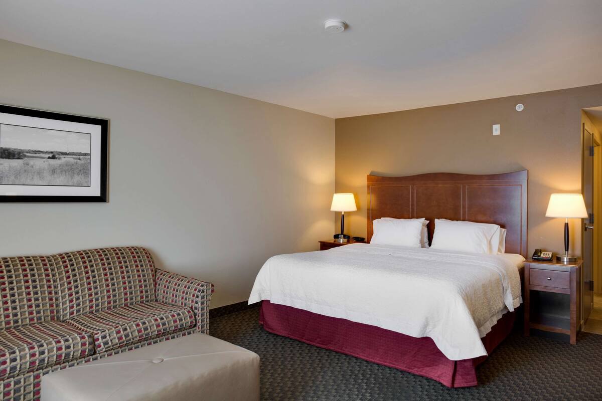 A hotel room with a bed, two bedside tables with lamps, a sofa, and a framed picture on the wall.