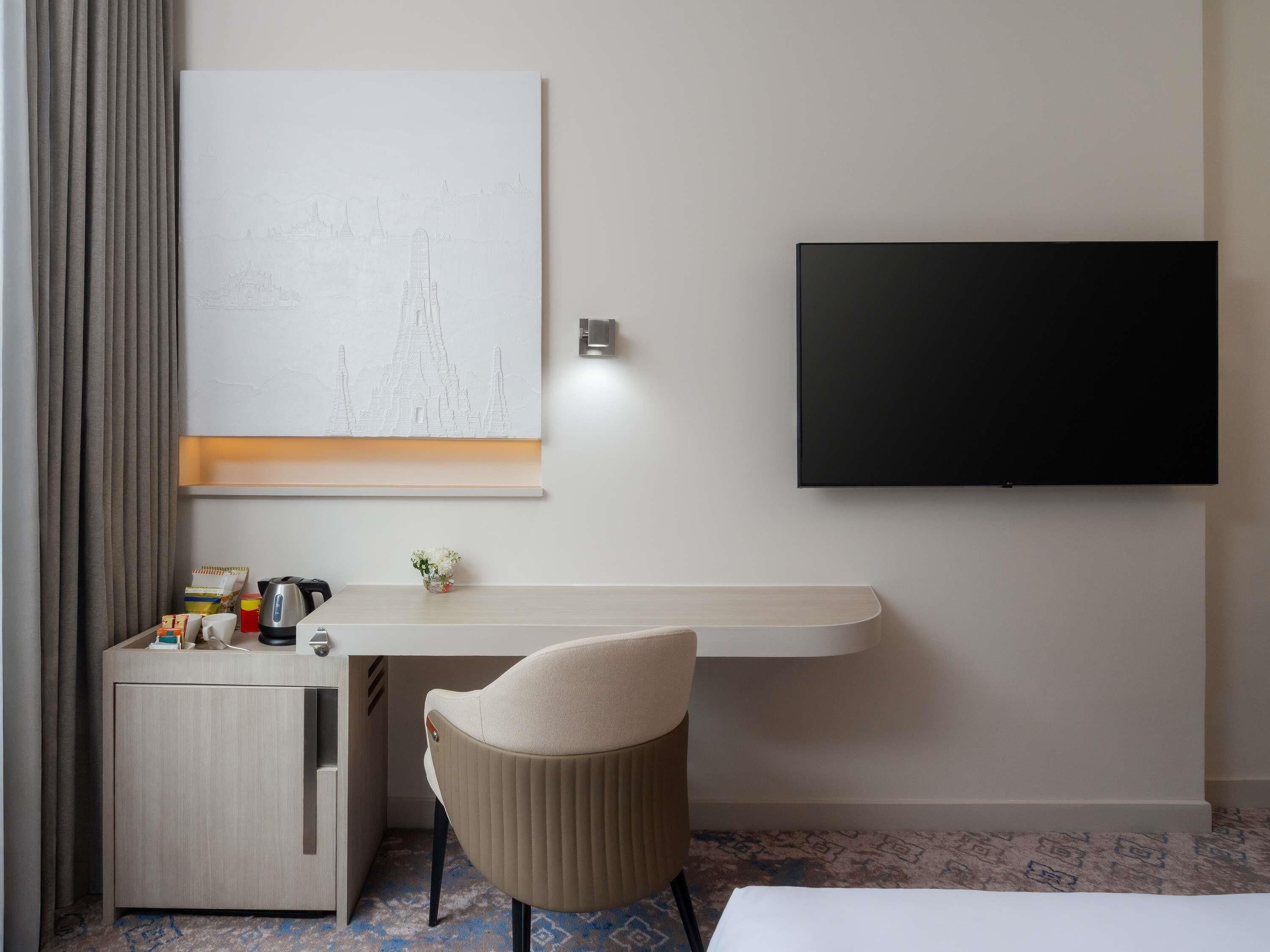 Ein Hotelzimmer mit Bett, Schreibtisch mit Stuhl, Flachbildfernseher, Wandkunst und einem kleinen Tisch mit Blumen.