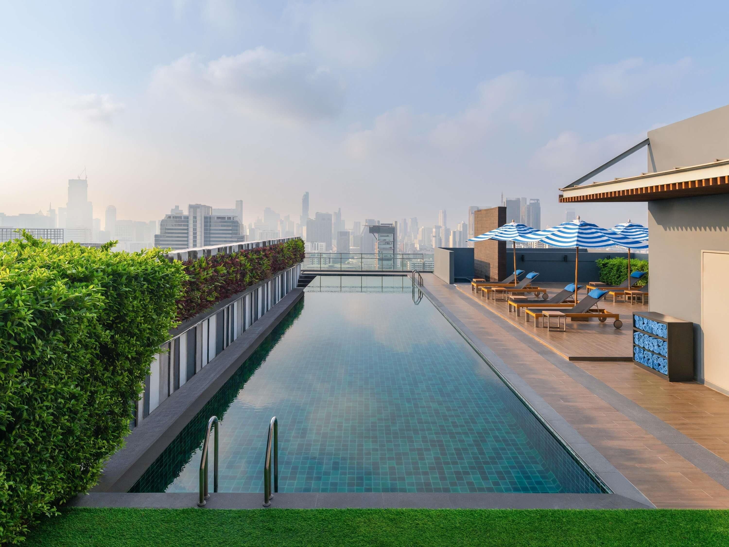 A rooftop infinity pool with a city skyline view, lounge chairs, and umbrellas.