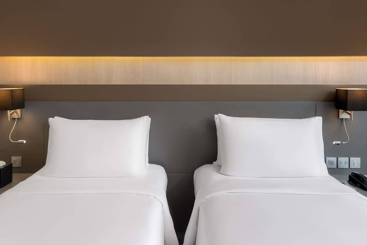 A hotel room with two single beds, a wooden headboard, bedside lamps, and a nightstand with a phone and a lamp.
