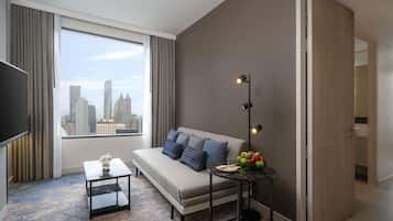 Una habitación de hotel moderna con un ventanal grande, un sofá, una mesita y una lámpara de pie.