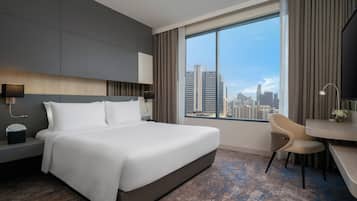 A modern hotel room with a large bed, a desk, and a view of the city skyline.