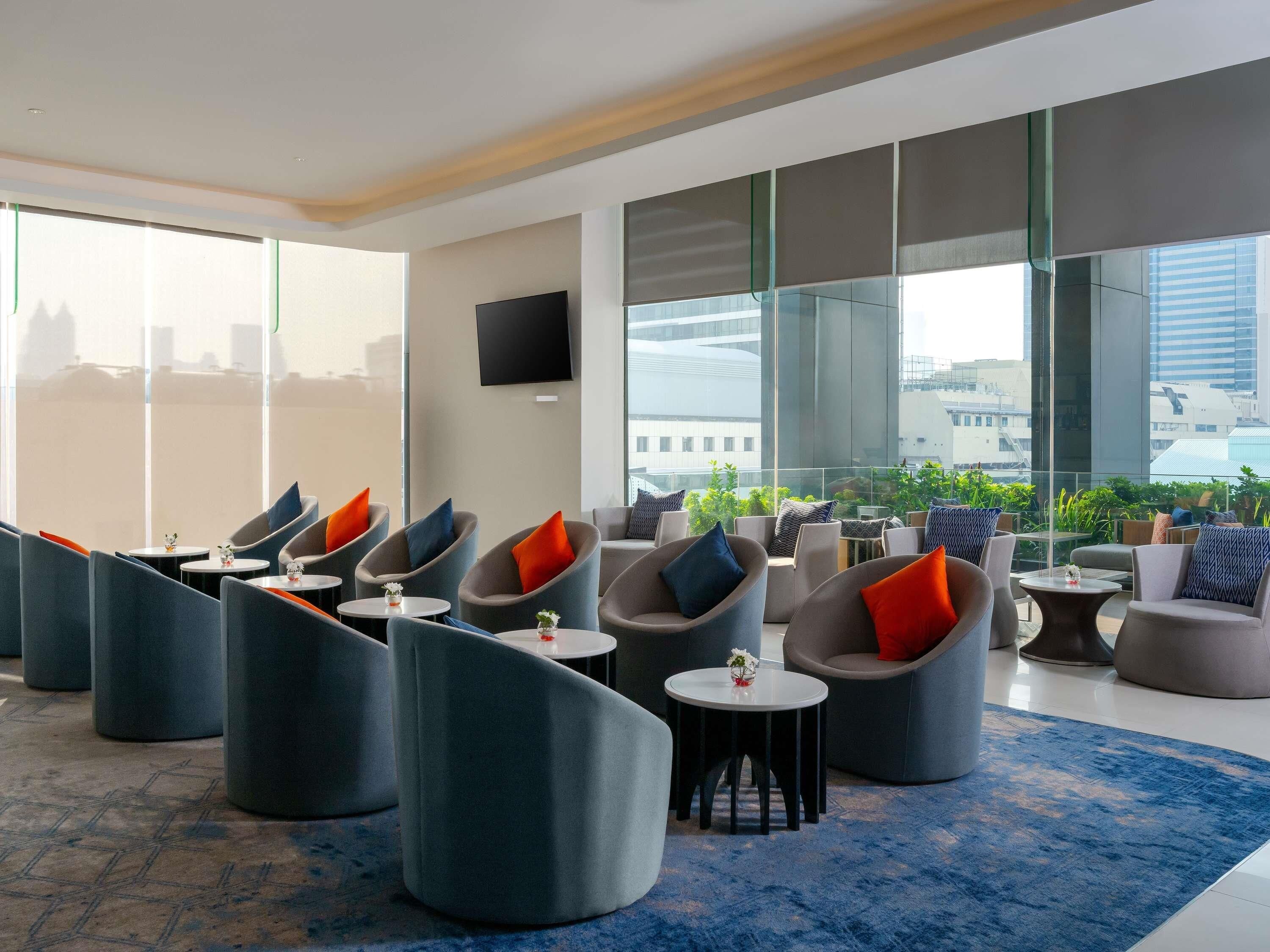 Un área de estar moderna con asientos curvos, un televisor de pantalla plana y ventanas amplias con vistas a la ciudad.