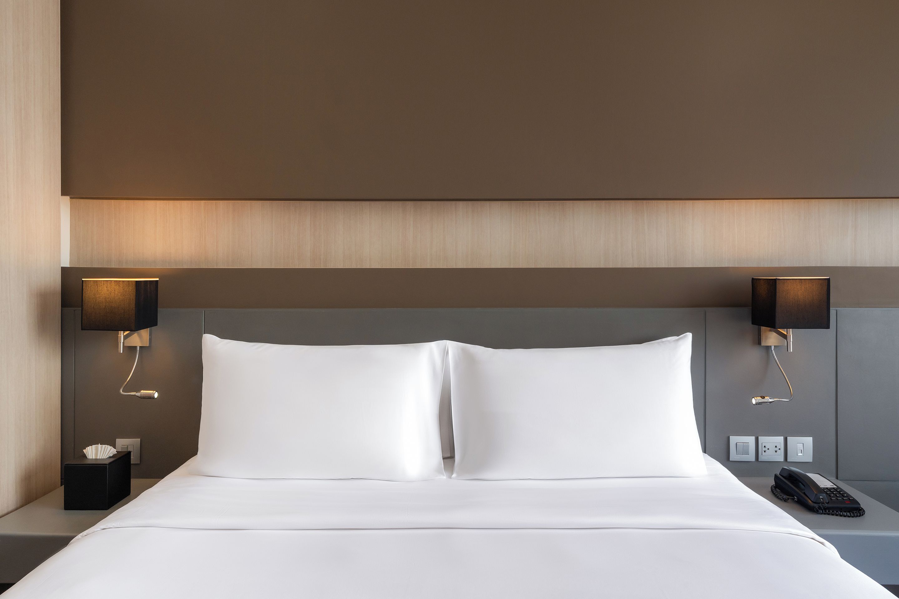 A hotel room with a large bed, two bedside lamps, a bedside telephone, and a small table with a tissue box.