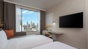 A hotel room with a bed, a desk, a chair, a TV, and a view of a cityscape.