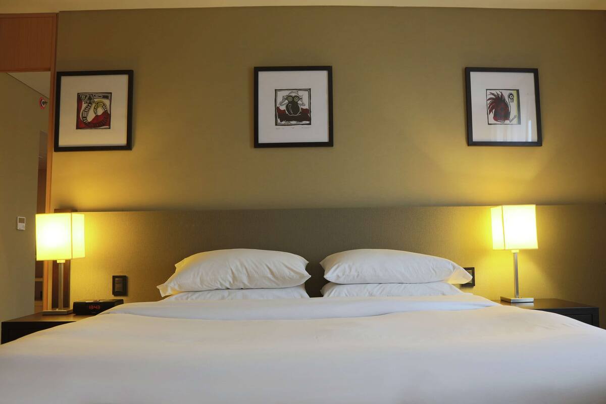 A hotel room with a large bed, two bedside lamps, and three framed artworks on the wall.