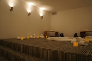 A spa room with a wooden floor, a bathtub, and several towels and candles. - Hilton Garden Inn Tucuman (San Miguel de Tucuman)