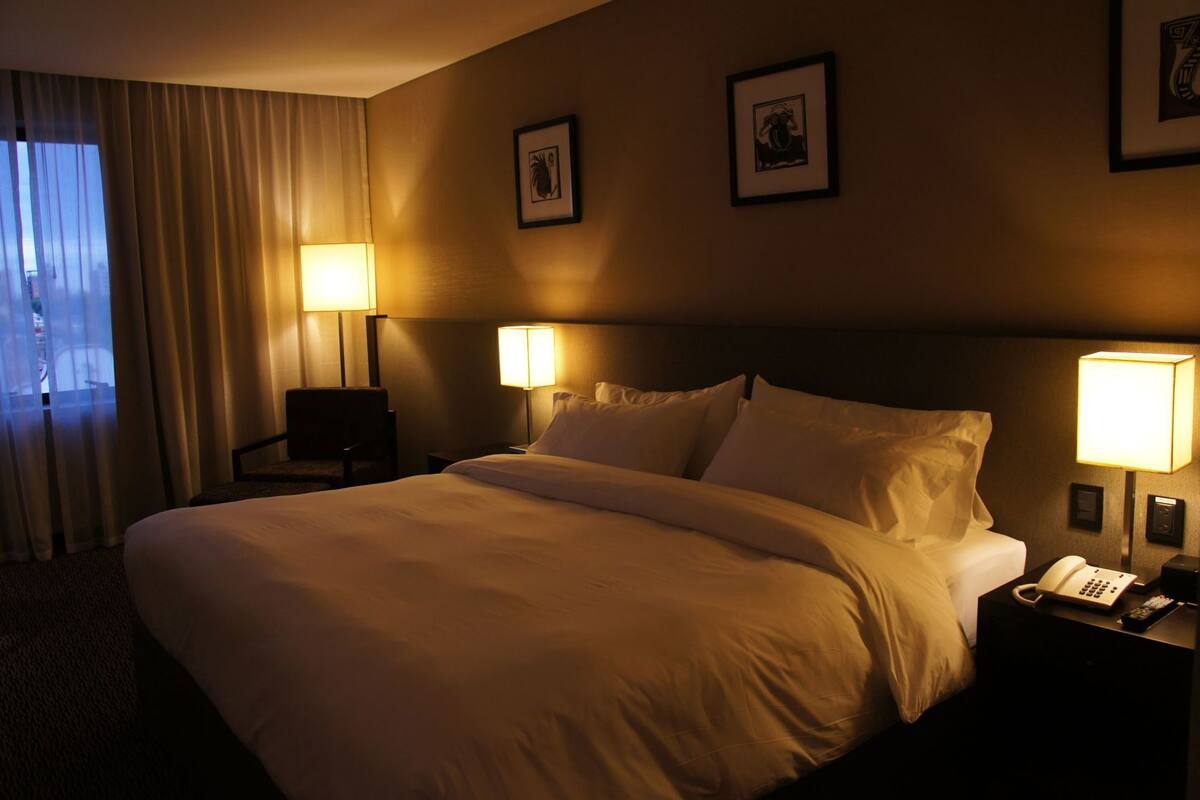 A hotel room with a large bed, two bedside lamps, a chair, and two framed pictures on the wall.