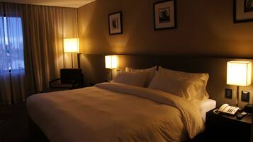 Una habitación de hotel con una cama grande, dos lámparas de noche, una mesita con teléfono y cuadros enmarcados en la pared.