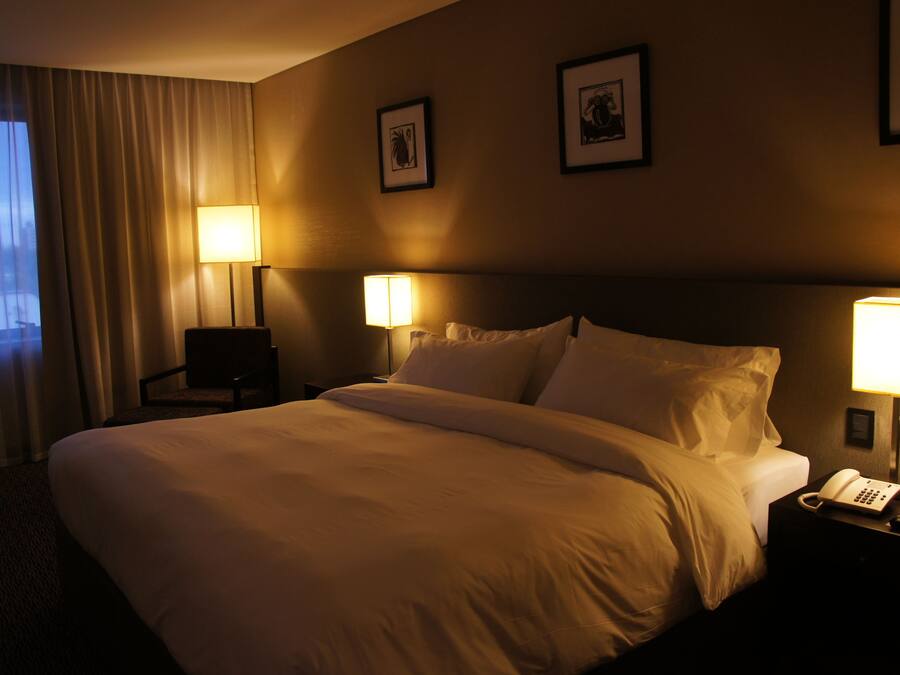 Una habitación de hotel con una cama grande, dos lámparas de noche, una mesita con teléfono y cuadros enmarcados en la pared.