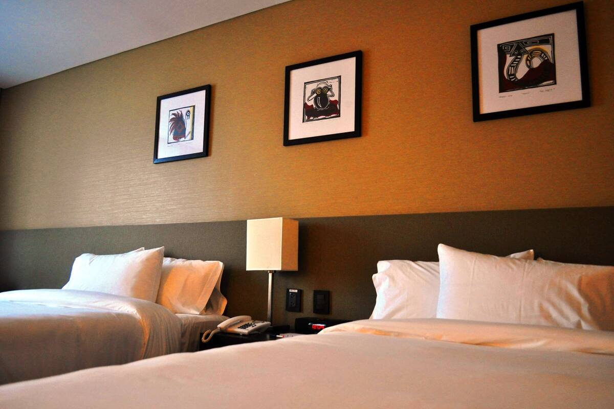 A hotel room with two beds, a nightstand with a lamp, and three framed pictures on the wall.