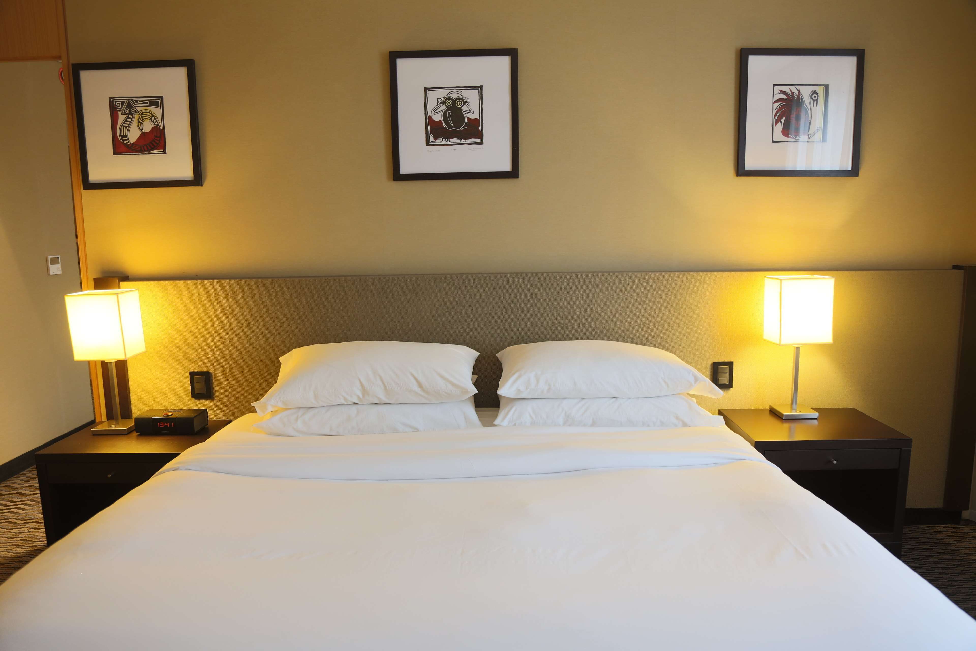 A hotel room with a large bed, two bedside tables, two lamps, and three framed pictures on the wall.