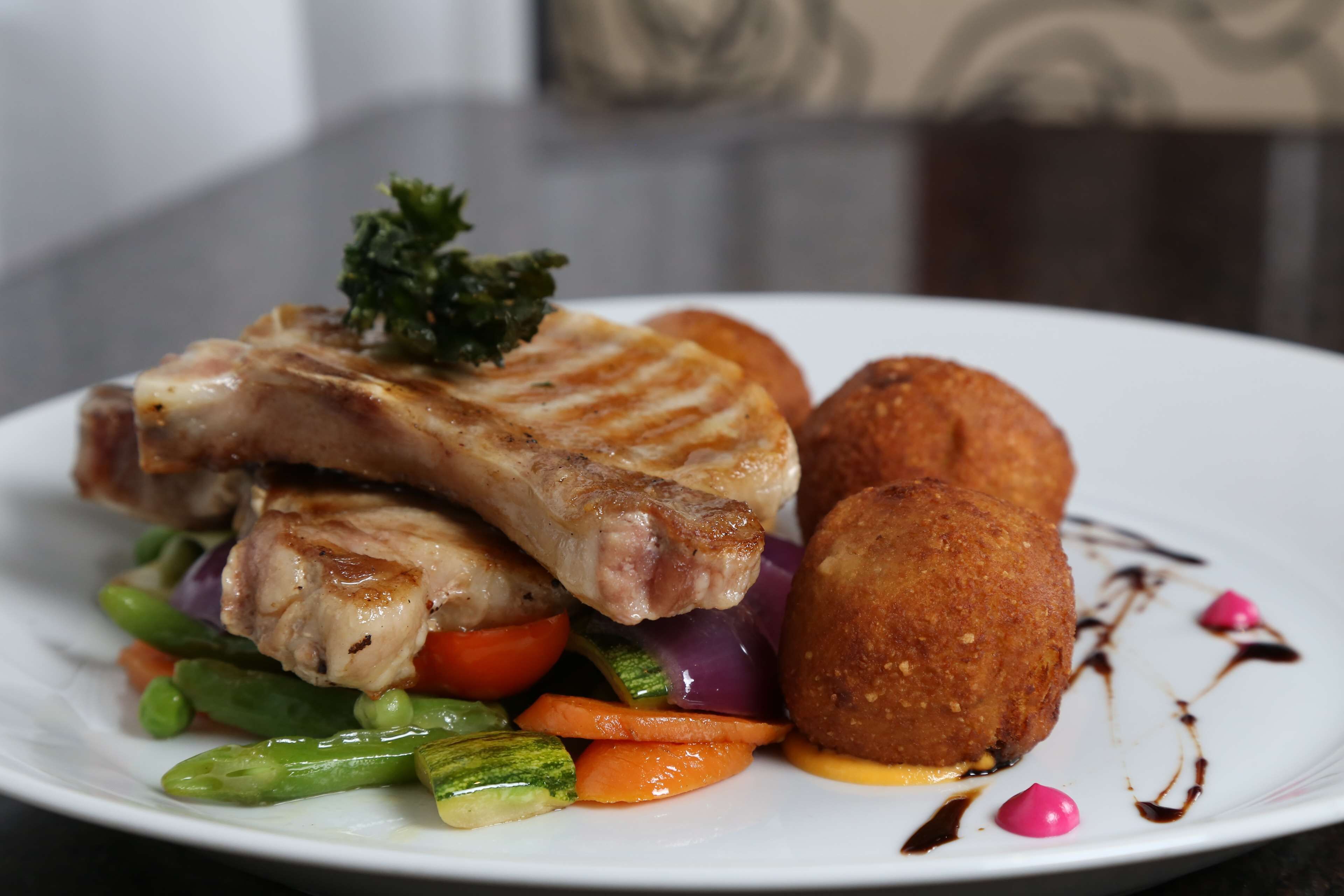A plate of food with grilled meat, vegetables, and a fried item, garnished with a sprig of parsley.