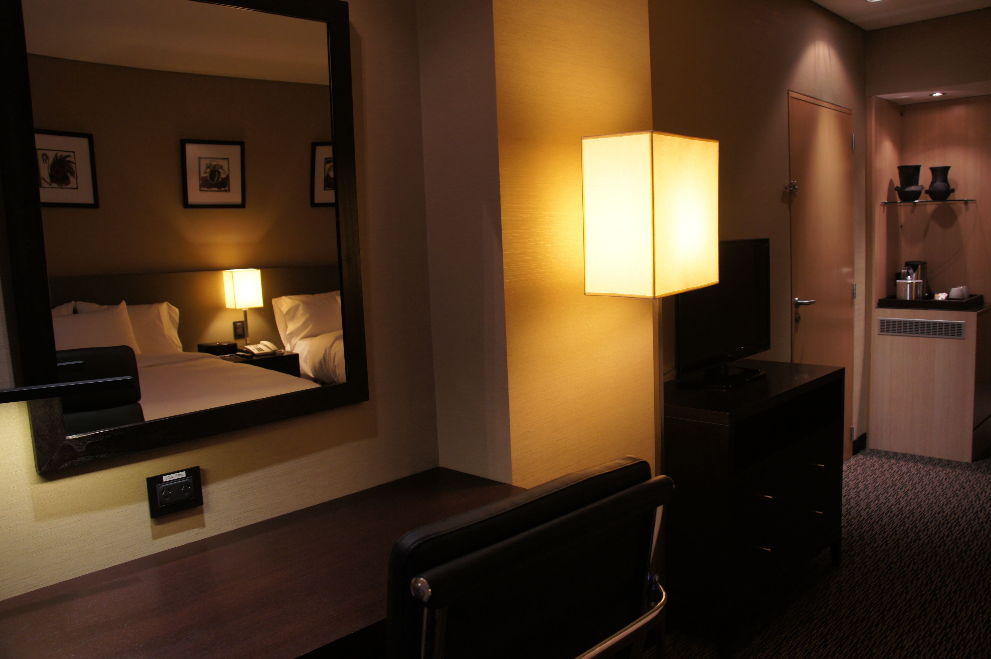 A hotel room with a large bed, a bedside lamp, a TV, a desk, and a mirror.