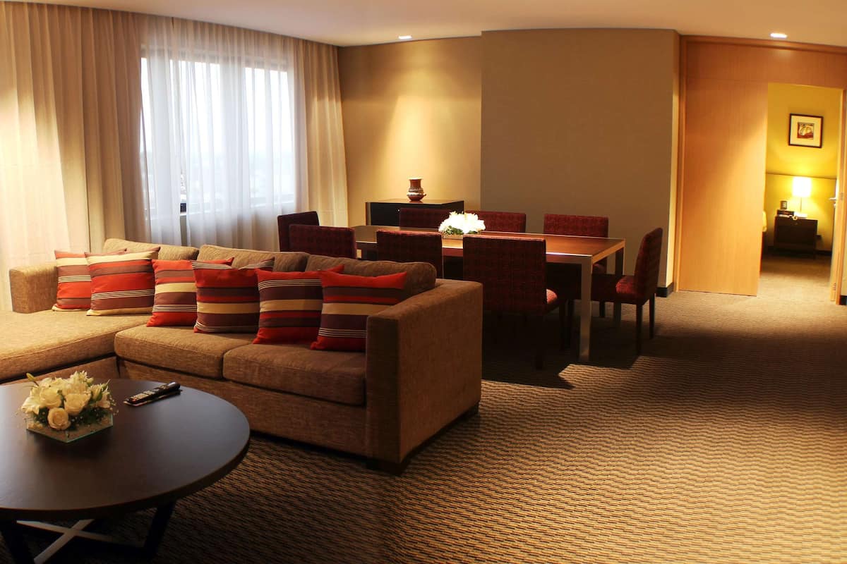 A hotel room with a sofa set, a dining table, and a lamp.
