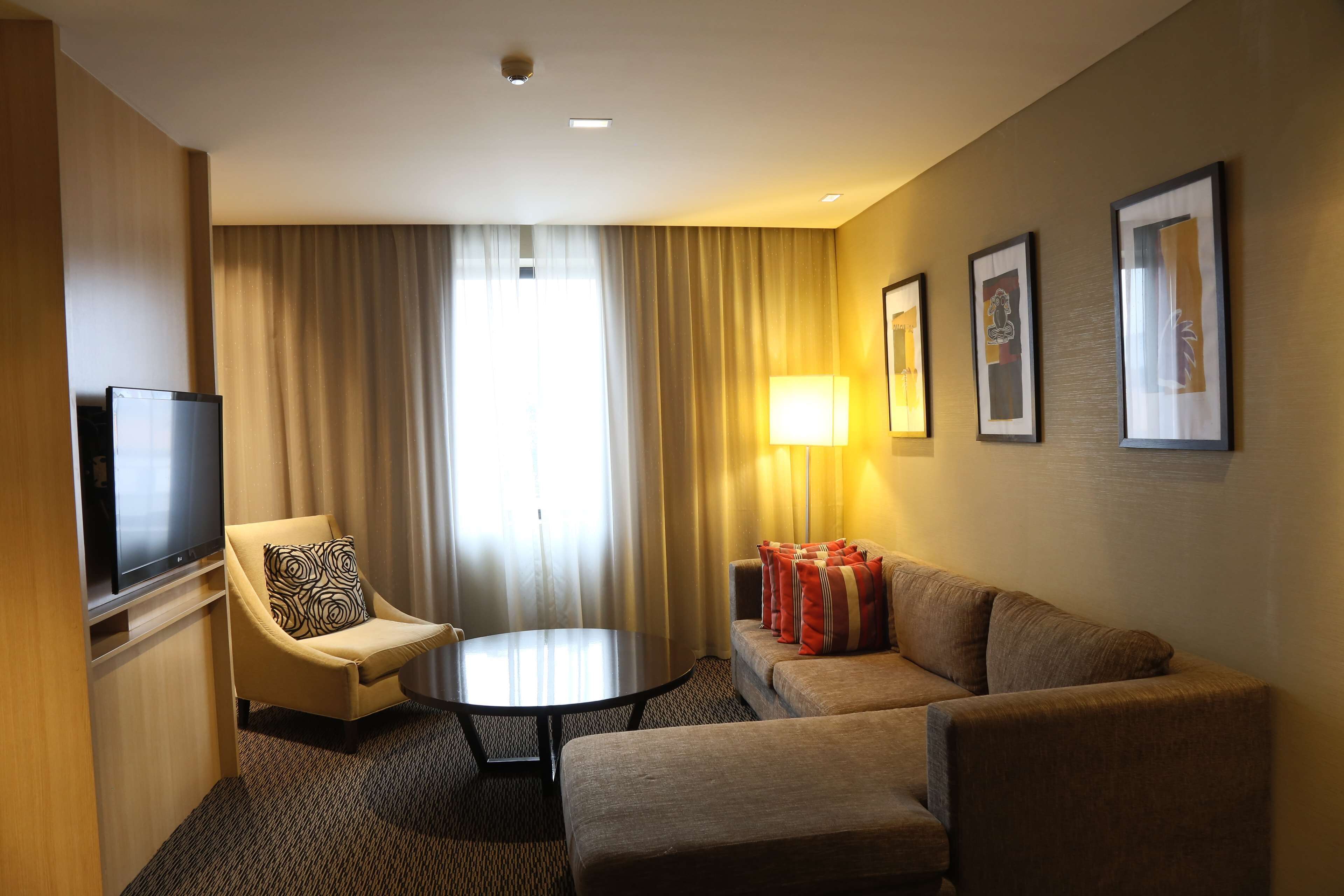 Habitación de hotel con sofá, sillón, televisor y lámpara.