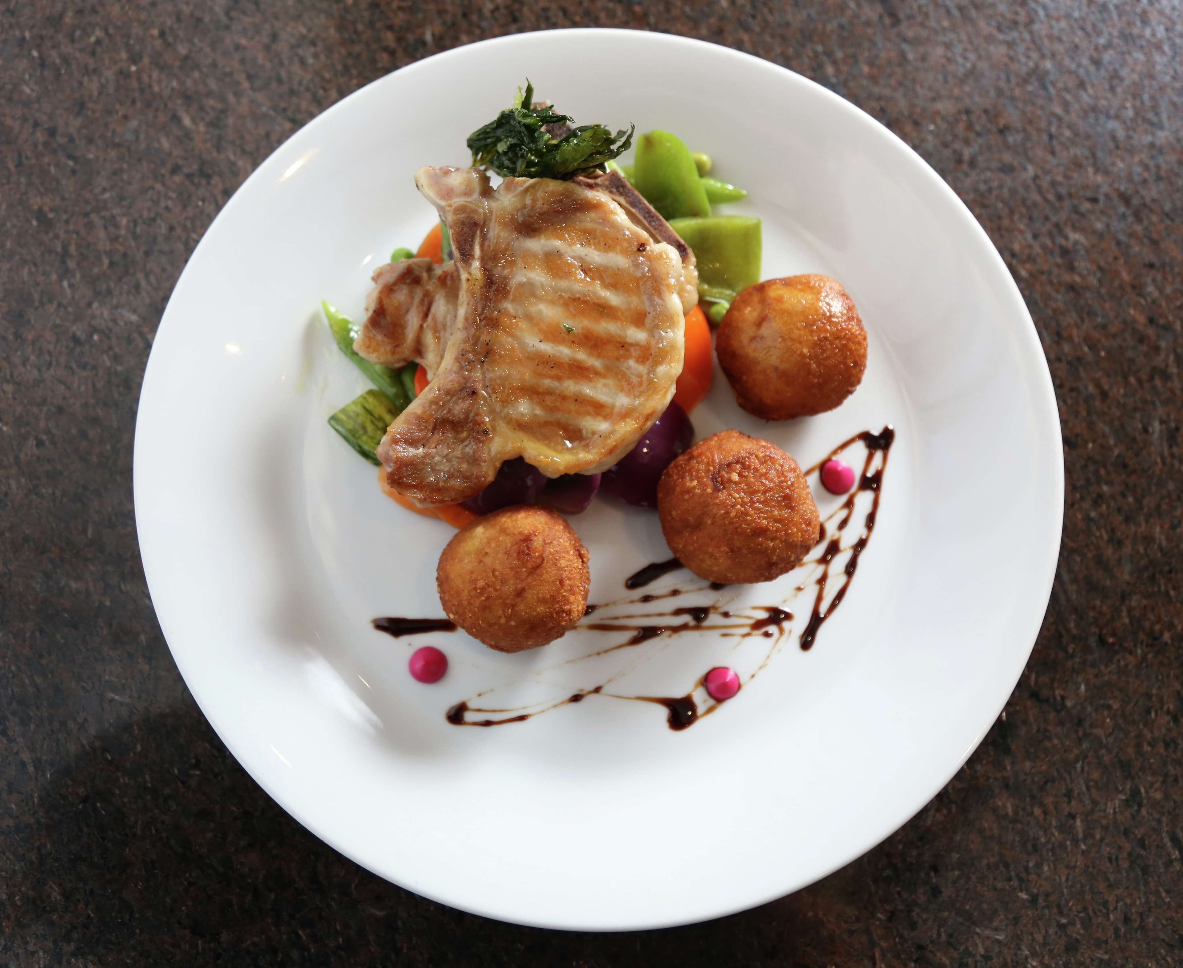 A plate with a piece of meat, vegetables, and two round items, possibly fried, on a dark countertop.