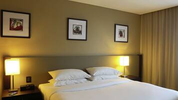 Una habitación de hotel con una cama bien hecha, dos lámparas de noche y tres cuadros en la pared.