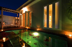 A swimming pool with rose petals, a covered seating area, and a building with large windows.