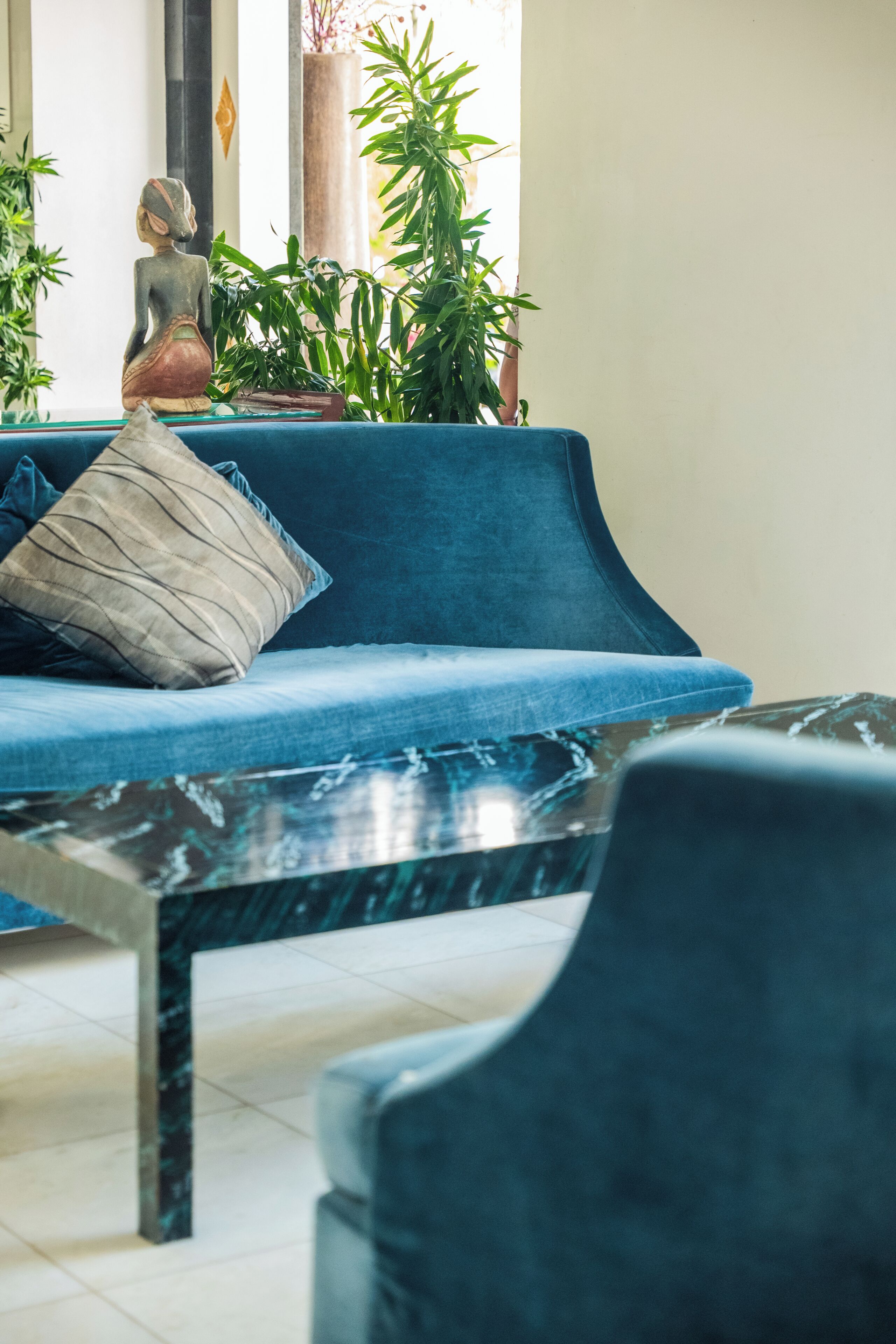 Een blauwe bank met een kussen, een marmeren tafel en een stoel in een kamer met een betegelde vloer.