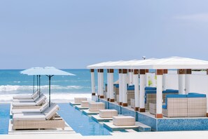 A poolside area with lounge chairs and umbrellas, a covered seating area, and a view of the ocean. - Lv8 Resort Hotel (Tibubeneng)