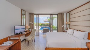 A hotel room with a bed, desk, chair, TV, and a view of a pool and garden.
