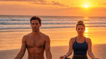 Two individuals meditating on a beach at sunset.