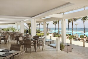 A spacious outdoor dining area with wicker furniture and a view of the beach and ocean. - Lv8 Resort Hotel (Canggu)