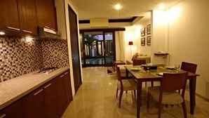 A modern kitchen with a tiled backsplash, wooden cabinets, and a dining area with a table and chairs. - Seminyak Townhouse Apartment (Legian)