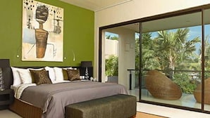 A modern bedroom with a large bed, a bench, a painting on the wall, and a view of palm trees through a glass door. - Seminyak Townhouse Apartment (Legian)