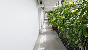 A corridor with tiled flooring, white walls, and potted plants along one side. - Seminyak Townhouse Apartment (Legian)