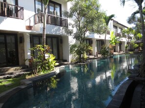 A swimming pool surrounded by lush greenery and modern buildings with balconies. - Seminyak Townhouse Apartment (Legian)
