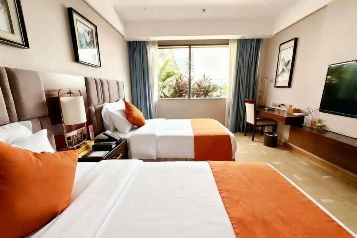A hotel room with two beds, a desk, a chair, a TV, and a window with curtains.