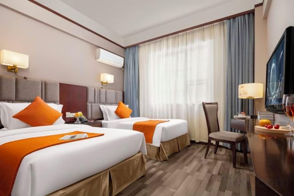 A hotel room with two beds, a desk, a chair, a TV, and a window with curtains.