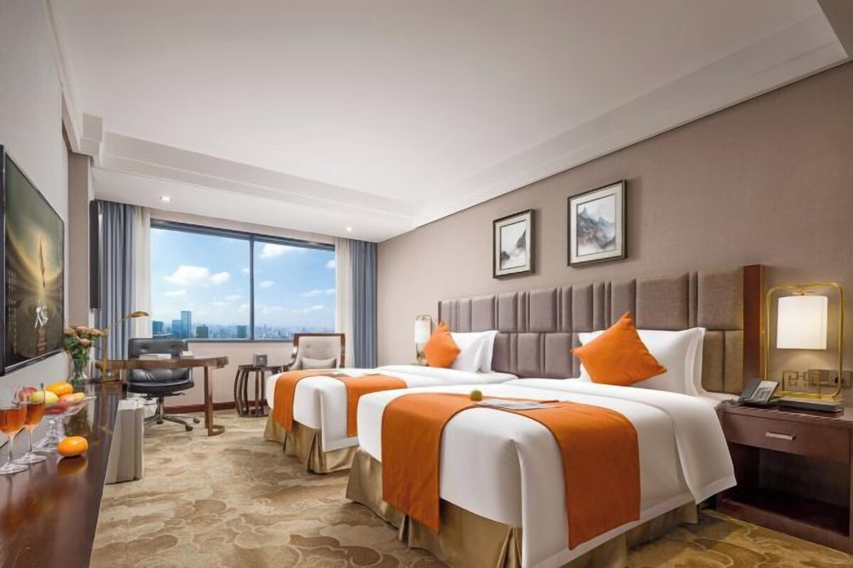 A hotel room with two beds, a desk, a chair, a city view, and a large window.
