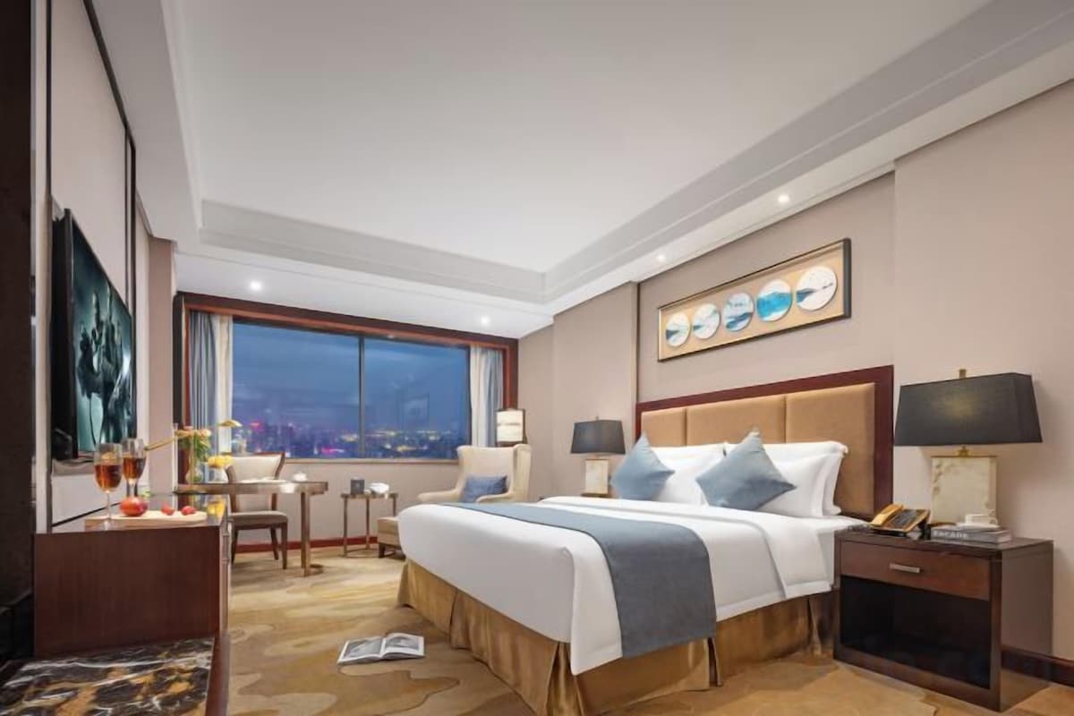 A hotel room with a large bed, bedside tables, a desk, and a view of the city at night.