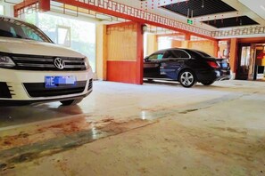 Un área de estacionamiento con dos coches, uno blanco y otro negro, y la entrada de un edificio con una decoración roja y blanca.